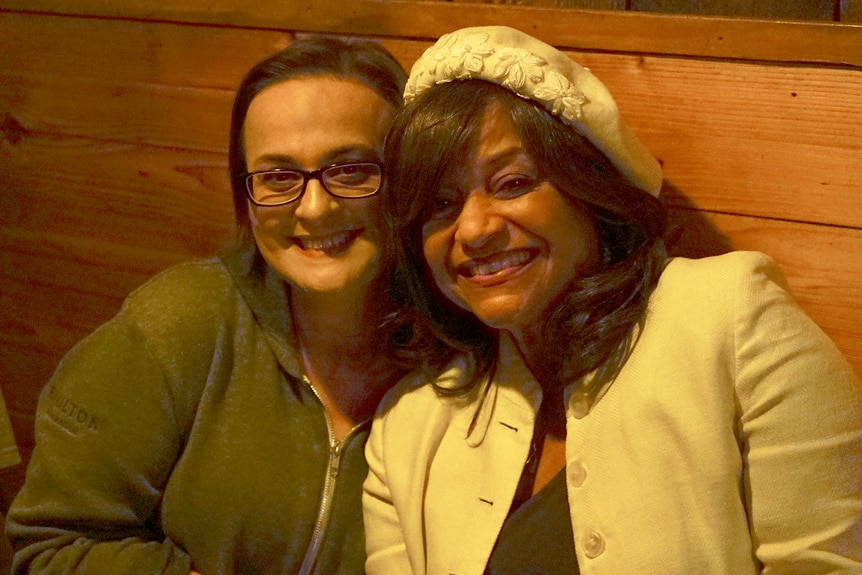 Elisabeth R Finch and Debbie Allen sit in a booth and smile together