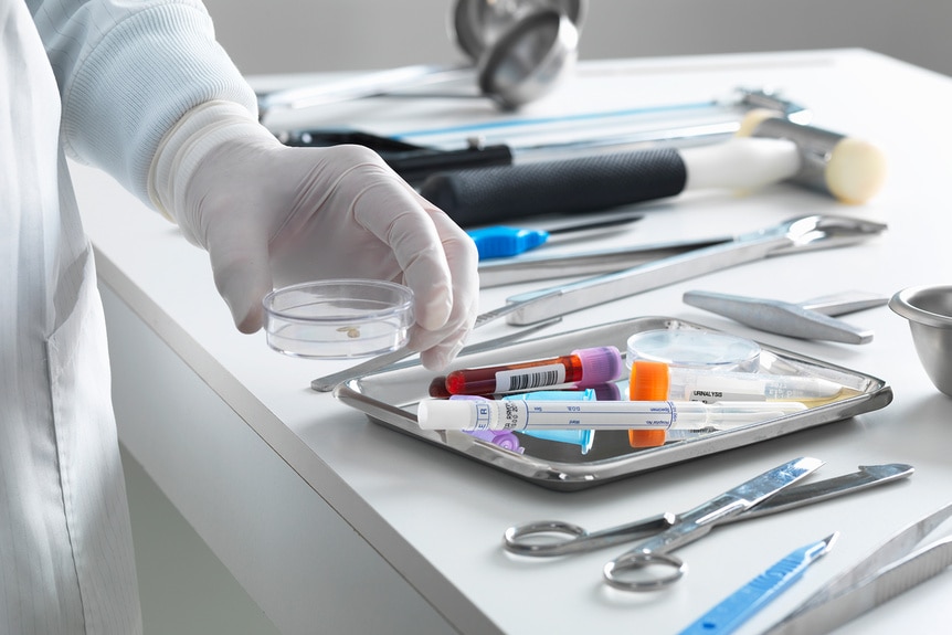 Medical Tools on a table with a doctors hand holding a sample